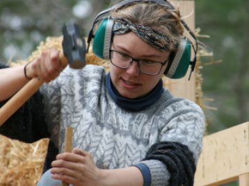 A woman wearing a head set uses a sludge hammer during construction.